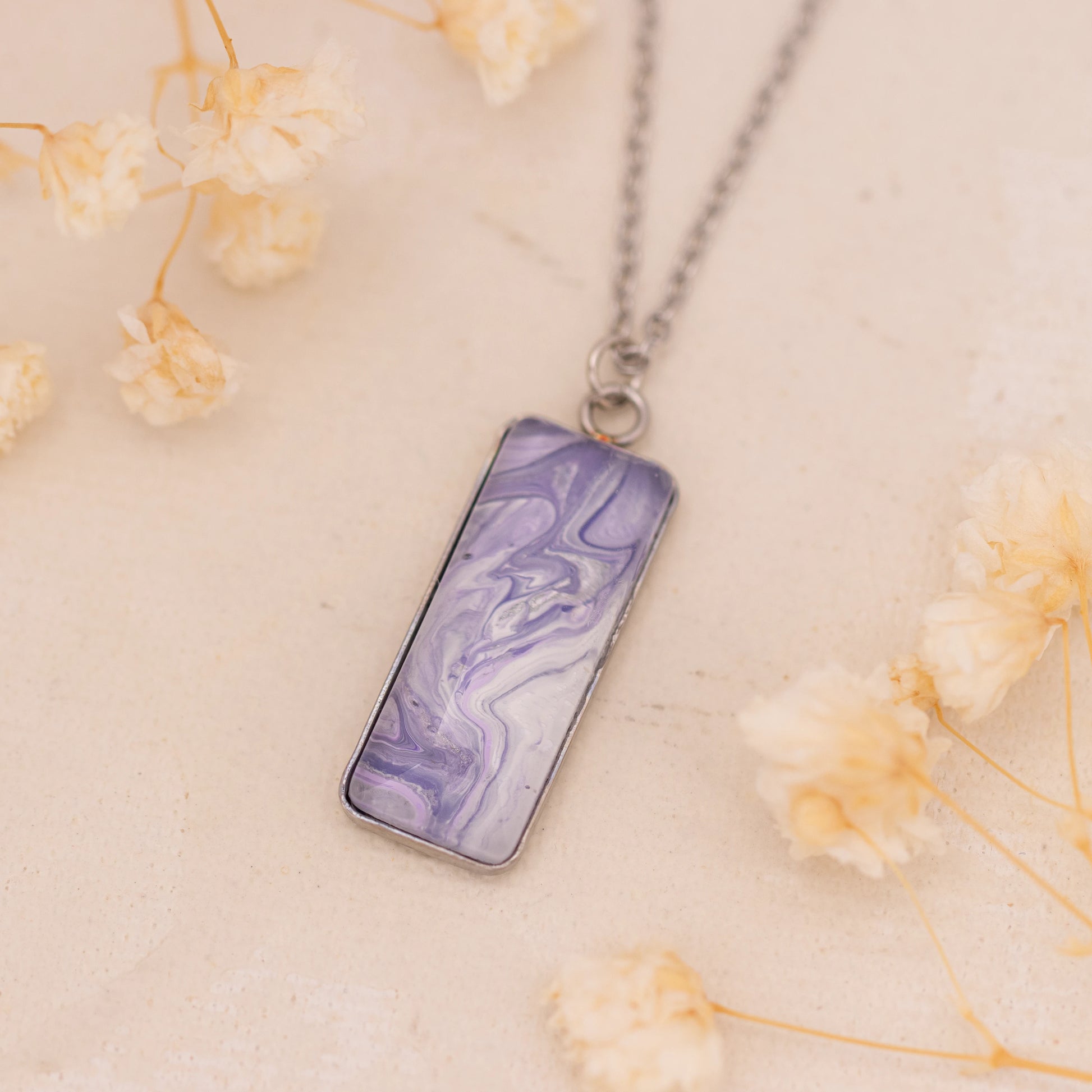 Dar Suad necklace featuring marbling artwork in purple and white with a stainless steel setting.