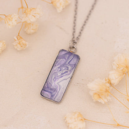 Dar Suad necklace featuring marbling artwork in purple and white with a stainless steel setting.